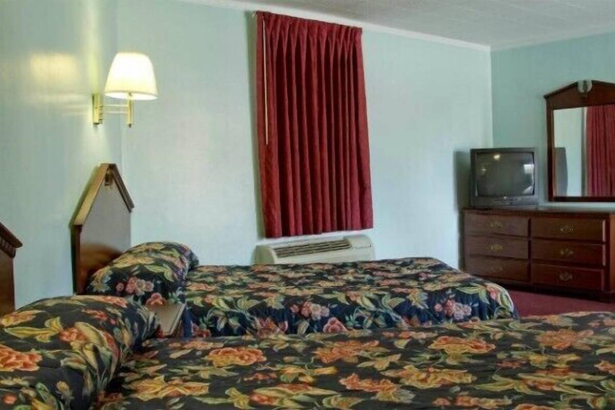 A hotel room with two beds, a television, a dresser, and a mirror.