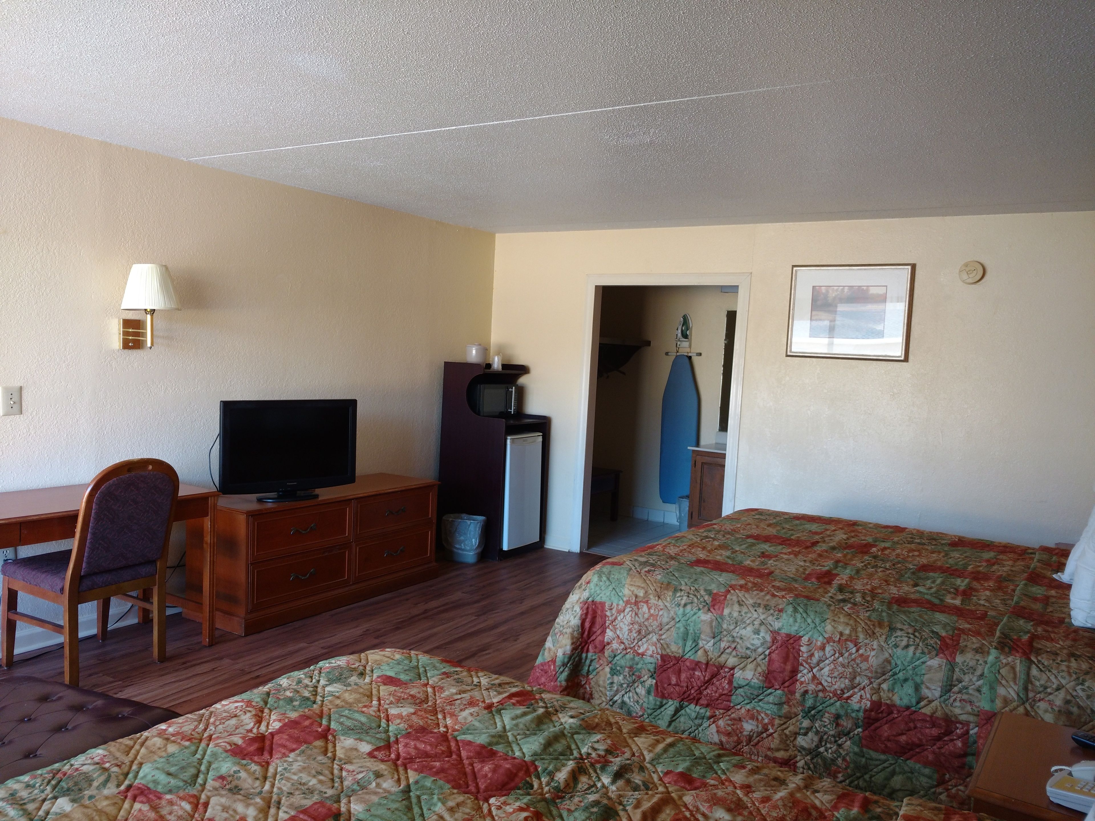 A hotel room with a bed, a desk with a television, a dresser, and a microwave.
