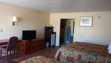 A hotel room with a bed, a desk with a television, a dresser, and a microwave.