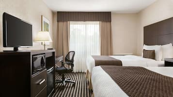 A hotel room with a bed, a desk with a television, a chair, and a window with curtains.