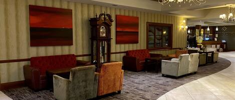 Een hotellobby met zithoeken, een grote klok en een receptiebalie.