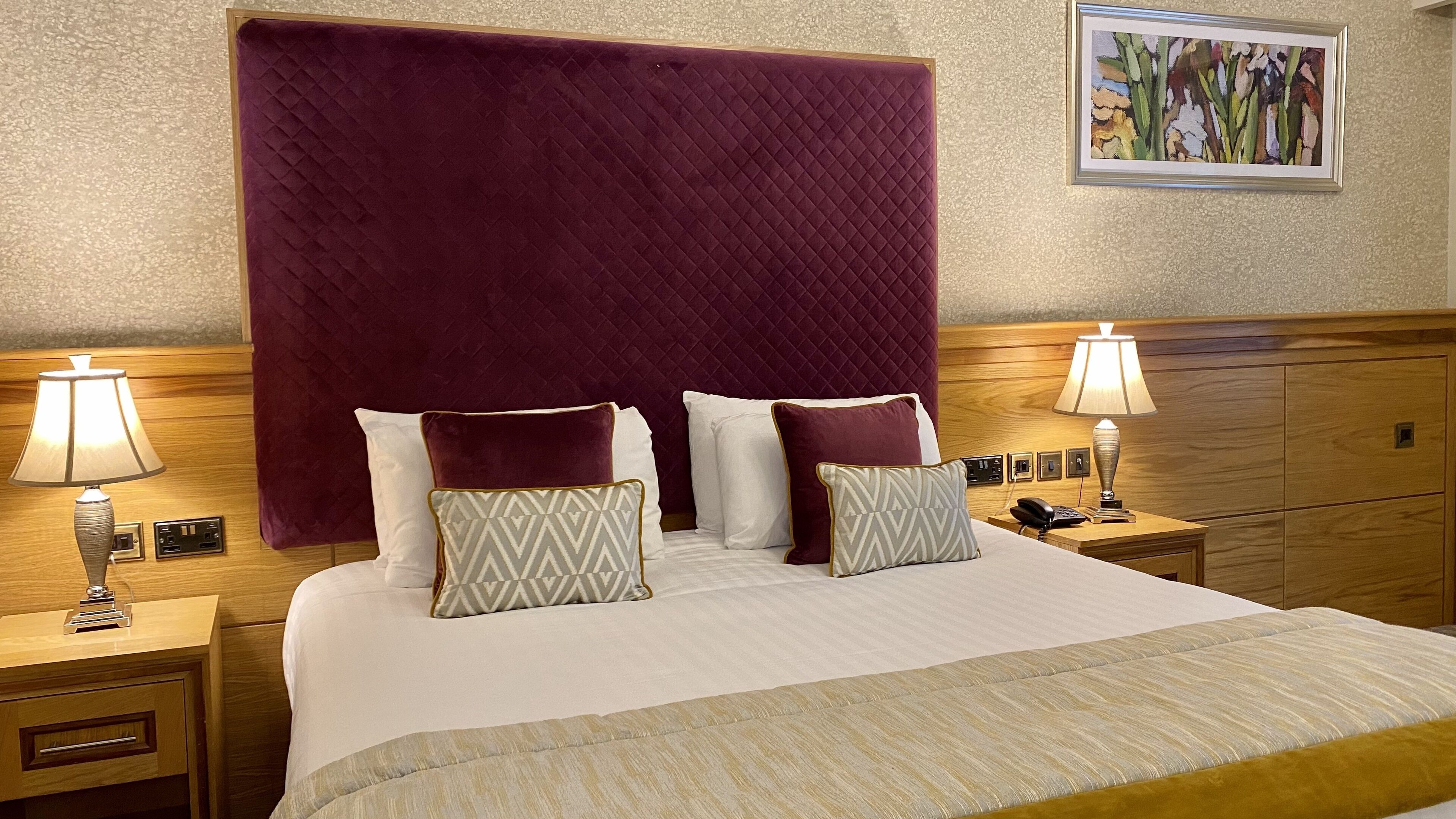 A hotel room with a large bed, two bedside tables, a wooden headboard, and a painting on the wall.