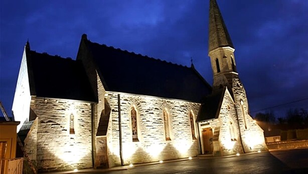A stone church with a tall spire and arched windows, illuminated at night. - An Grianan Hotel (Burt)