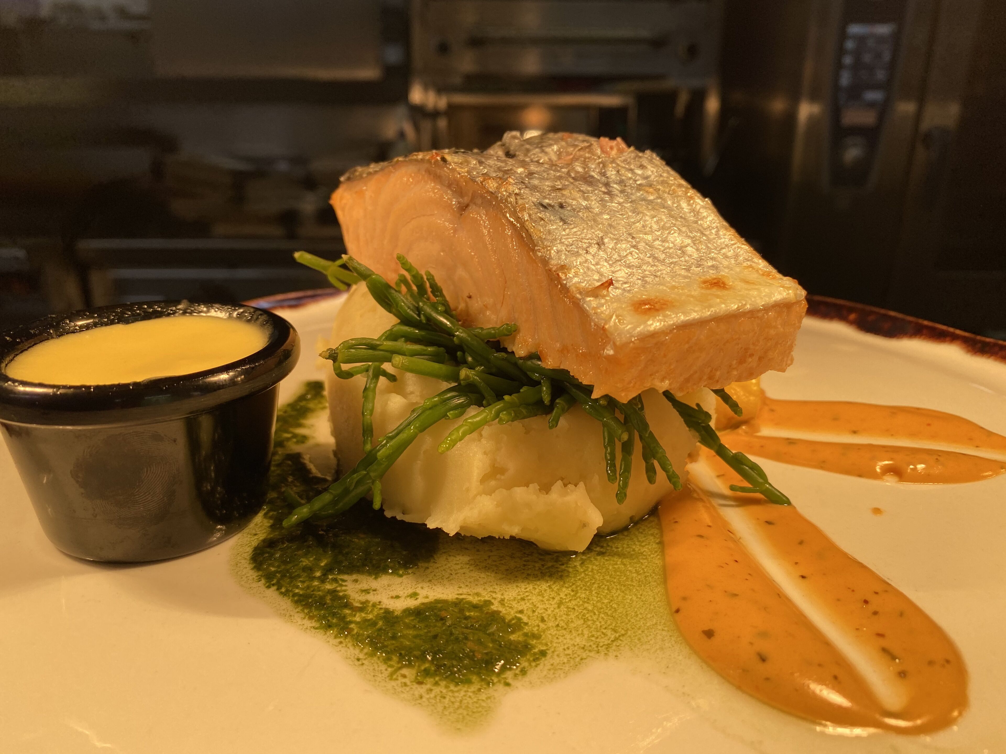 Prato com um pedaço de peixe, ervas verdes e molho.