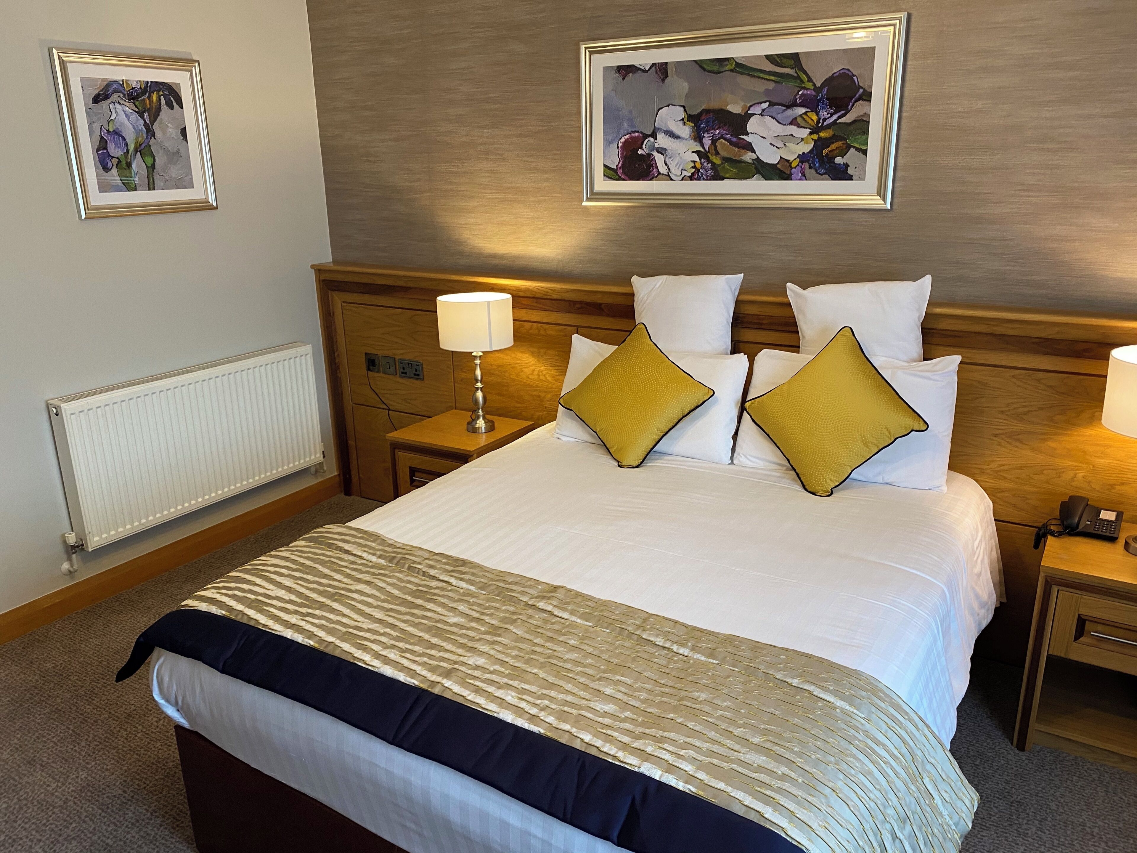 A hotel room with a bed, a nightstand, a lamp, and two framed floral paintings on the wall.