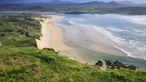 A coastal landscape with a sandy beach, grassy hills, and a view of distant mountains. - An Grianan Hotel (Burt)