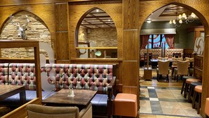A restaurant with wooden arches, a stone wall, and a plaid upholstered booth. Tables and chairs are arranged for dining. - An Grianan Hotel (Burt)
