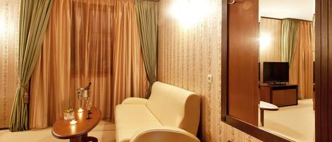A hotel room with a sofa, a small table with a candle, a mirror, and a television.