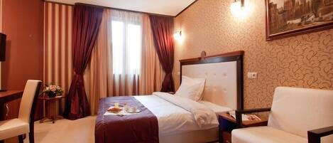 A hotel room with a bed, a chair, a desk, and a nightstand.
