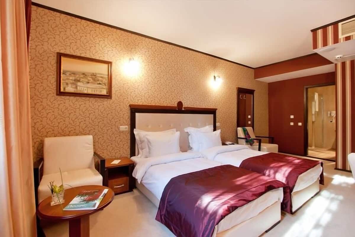 A hotel room with two beds, a sitting area with a chair and a table, and a large mirror.