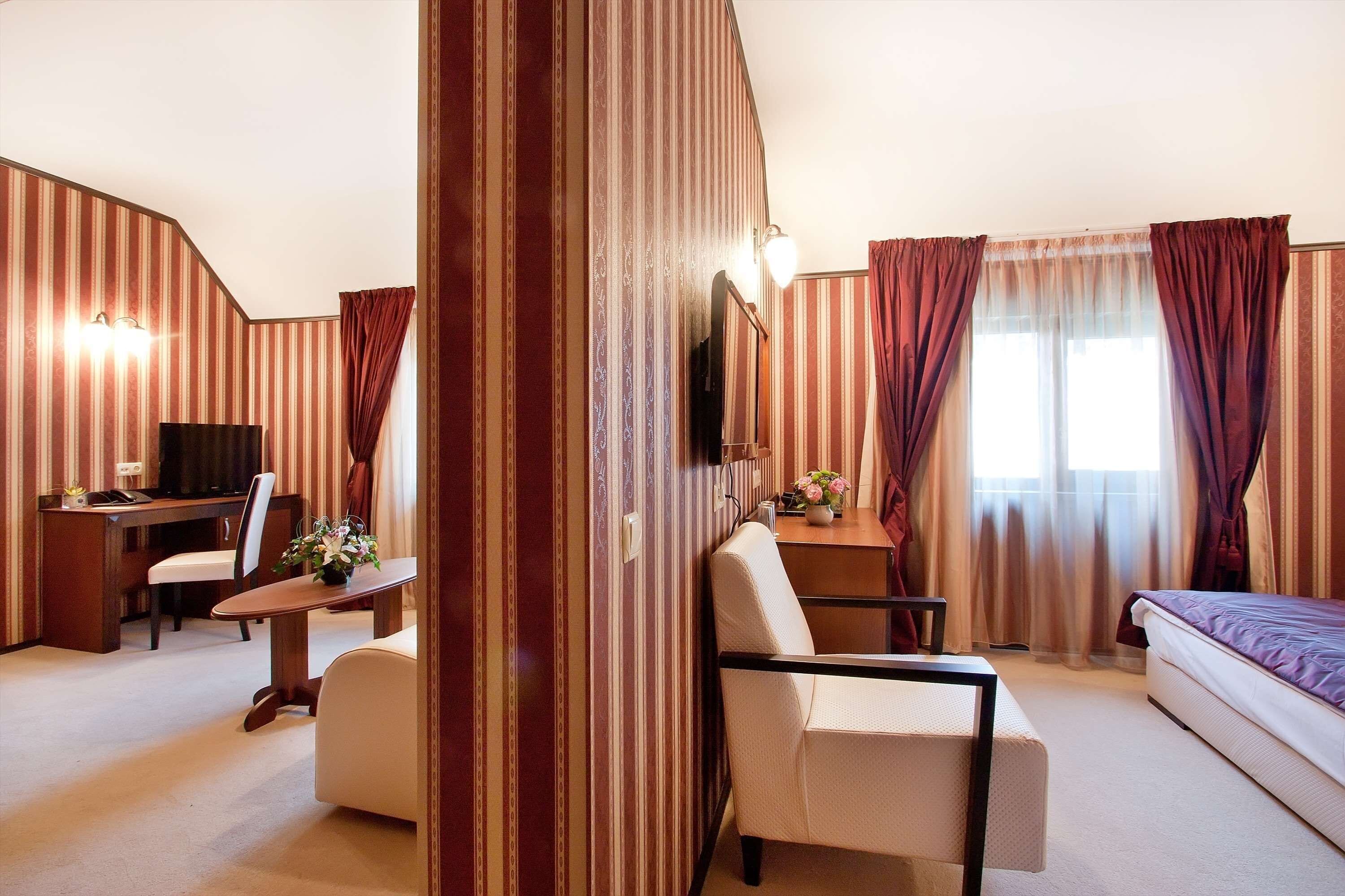 A hotel room with a bed, a desk, a chair, a small table with a vase of flowers, and a television.