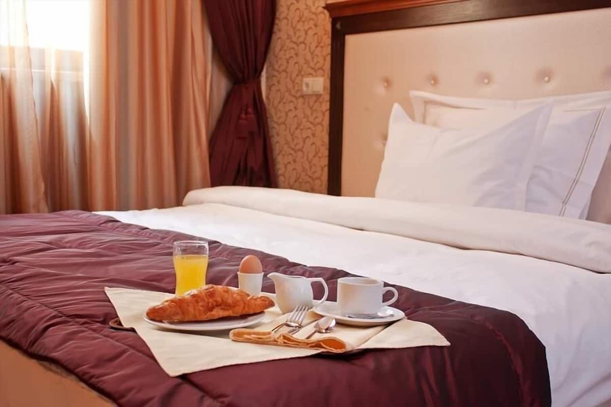A neatly made bed with a breakfast tray including croissants, orange juice, and coffee.