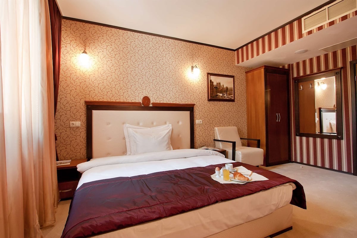 A hotel room with a large bed, a chair, a wardrobe, and a mirror.