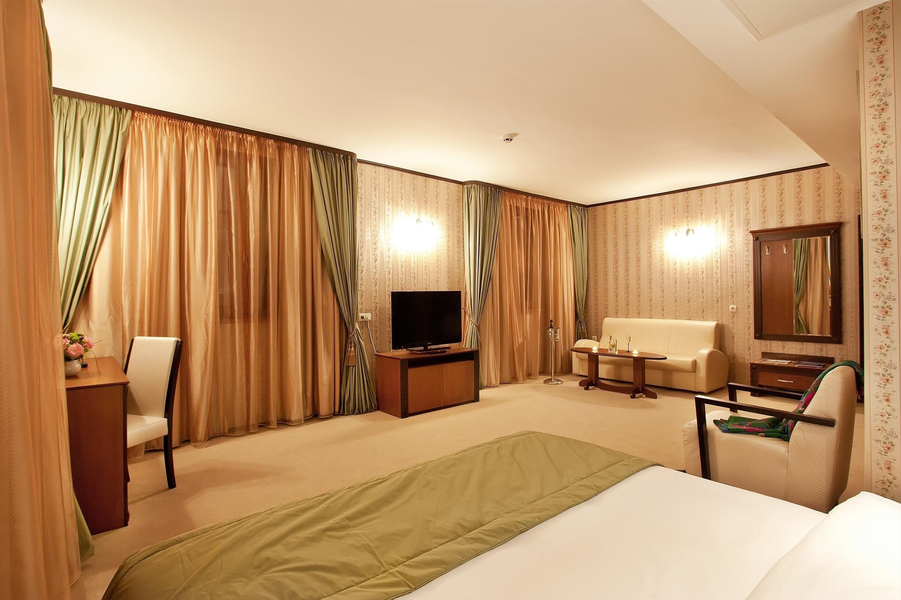 Une chambre d’hôtel équipée d’un lit, d’une télévision, d’un bureau, d’une chaise, d’un canapé et d’un miroir.