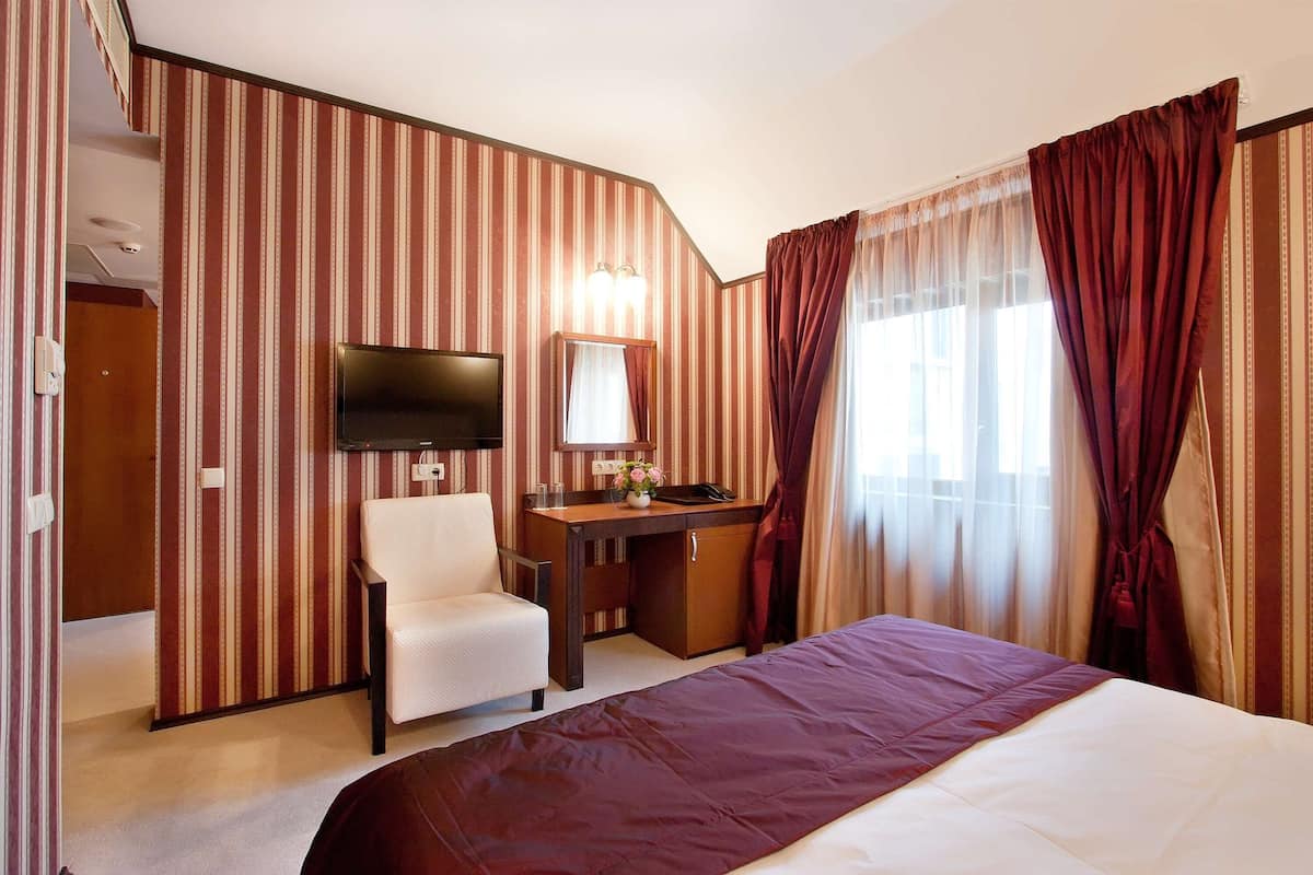 A hotel room with a bed, a desk with a mirror, a chair, a TV, and curtains.