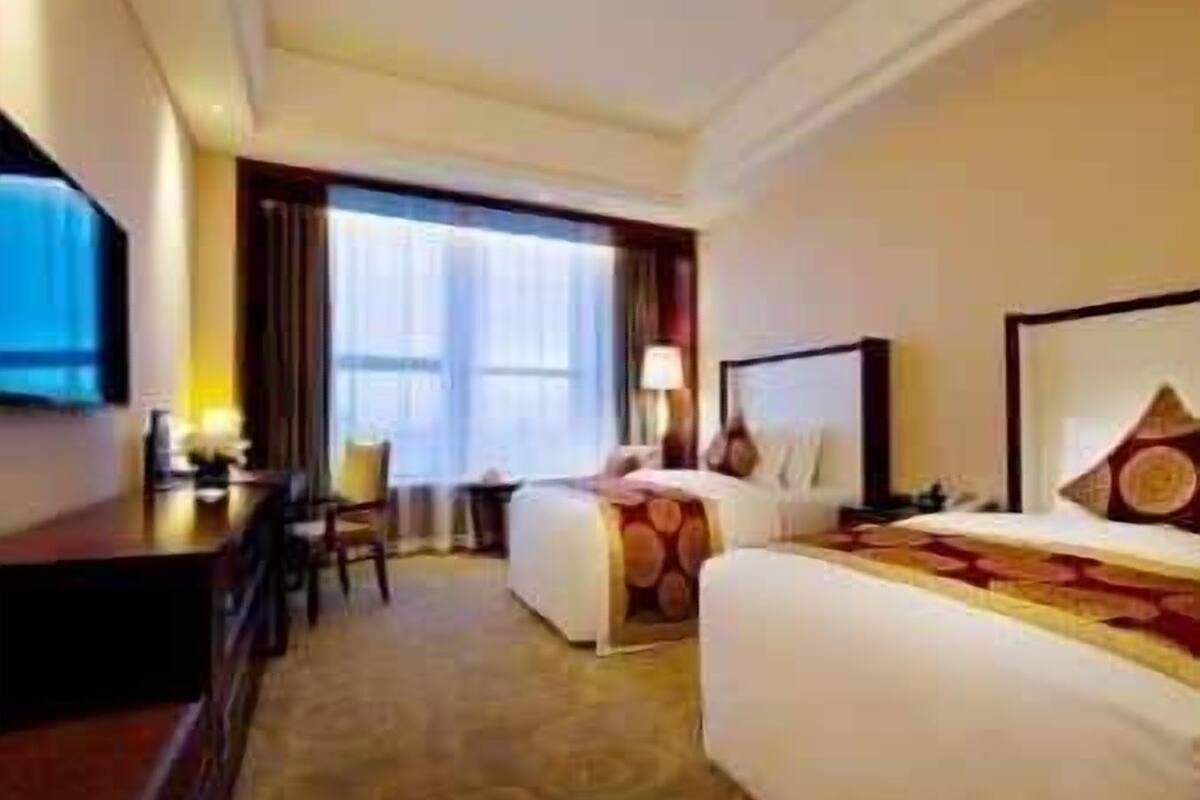 A hotel room with a bed, a desk, a chair, and a large window.