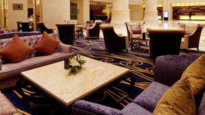 Un hall d’entrée spacieux, doté de hauts plafonds, de grandes colonnes et d’un espace salon central avec des canapés et une table basse.