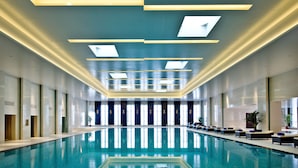 Une grande piscine intérieure au design moderne, caractérisée par une forme longue et étroite et une plateforme de plongeon centrale.