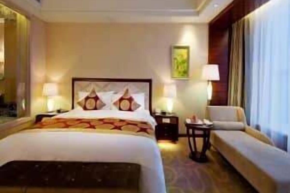 A hotel room with a large bed, a sofa, two bedside tables with lamps, and a painting on the wall.