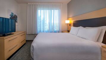 Une chambre d’hôtel avec un grand lit, un téléviseur posé sur une commode en bois, une fenêtre avec des rideaux et une lampe fixée au mur.