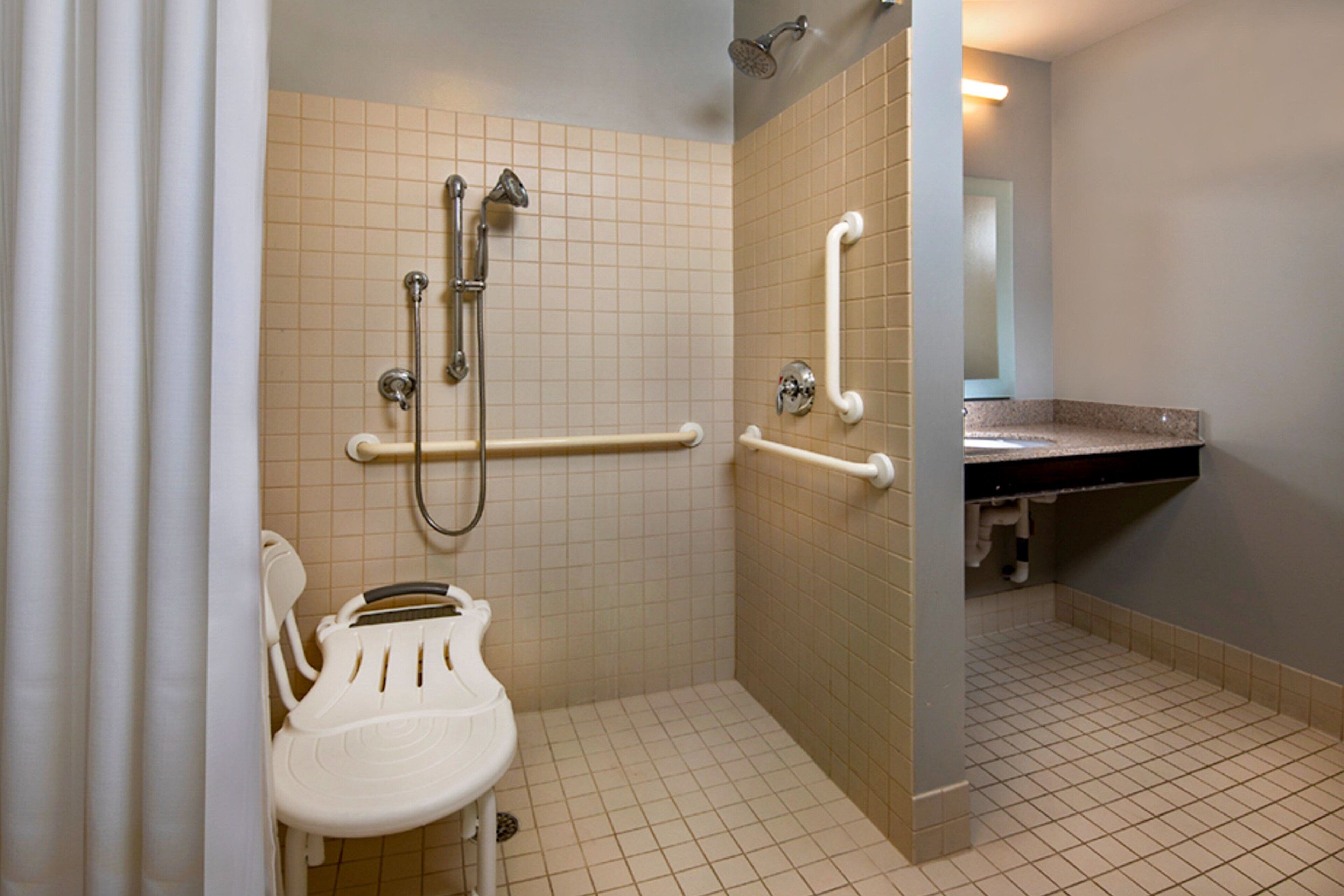 A bathroom with a wheelchair-accessible shower, grab bars, and a white toilet.