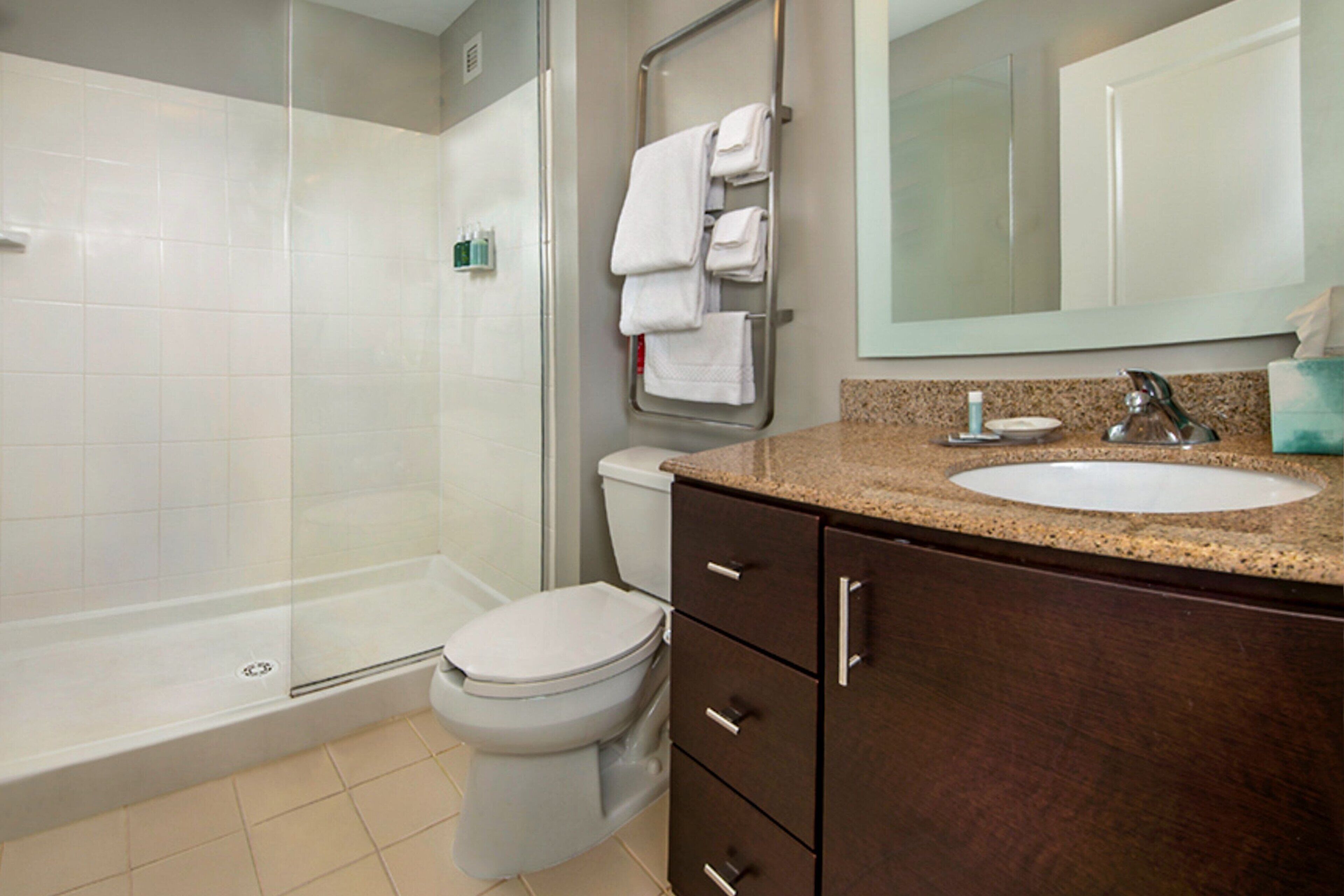 A bathroom with a shower, toilet, sink, and a towel rack with multiple towels.
