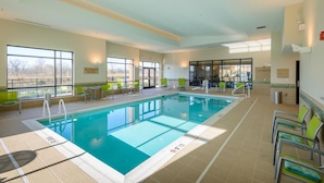 An indoor swimming pool with clear lanes, green chairs, and large windows offering a view of the outdoors. - TownePlace Suites by Marriott Frederick (Frederick)