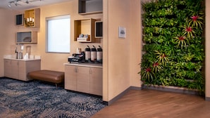 A modern hotel room with a large window, built-in shelves, a coffee station, a seating area, and a vertical garden wall. - TownePlace Suites by Marriott Frederick (Frederick)