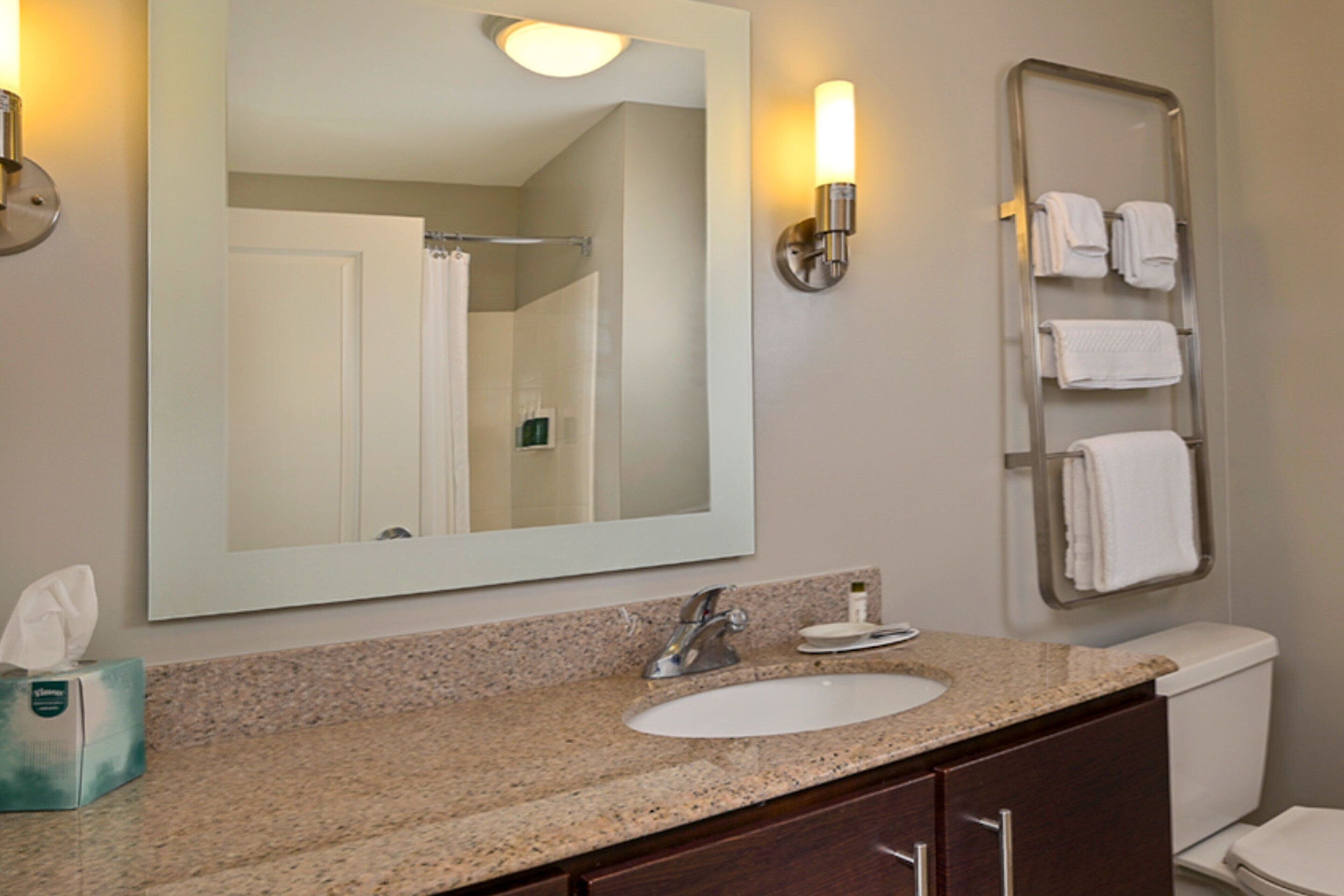 A bathroom with a granite countertop sink, a large mirror, a towel rack, and a toilet.