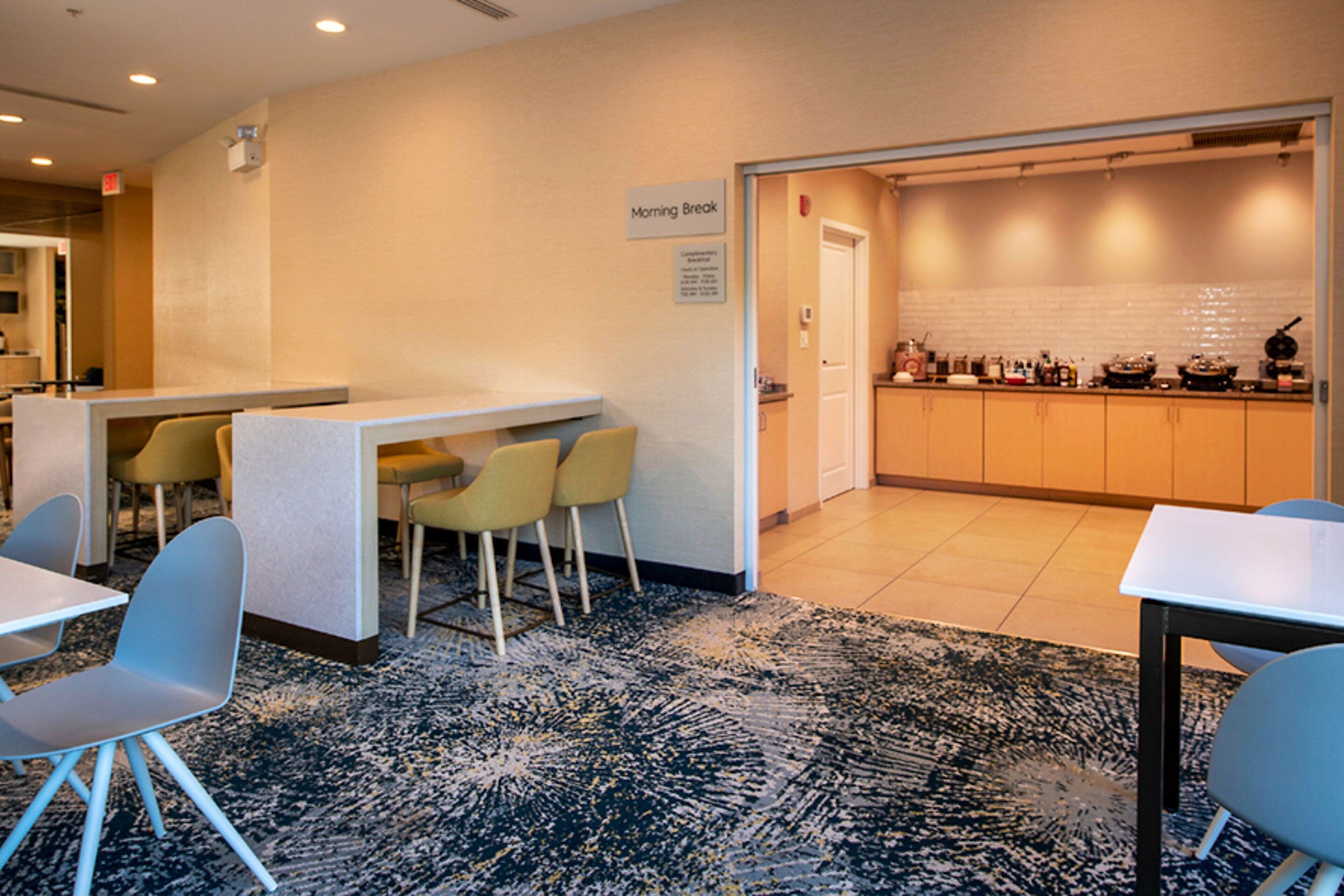 A modern hotel lobby with a reception desk, seating area, and a kitchen visible through an open door.