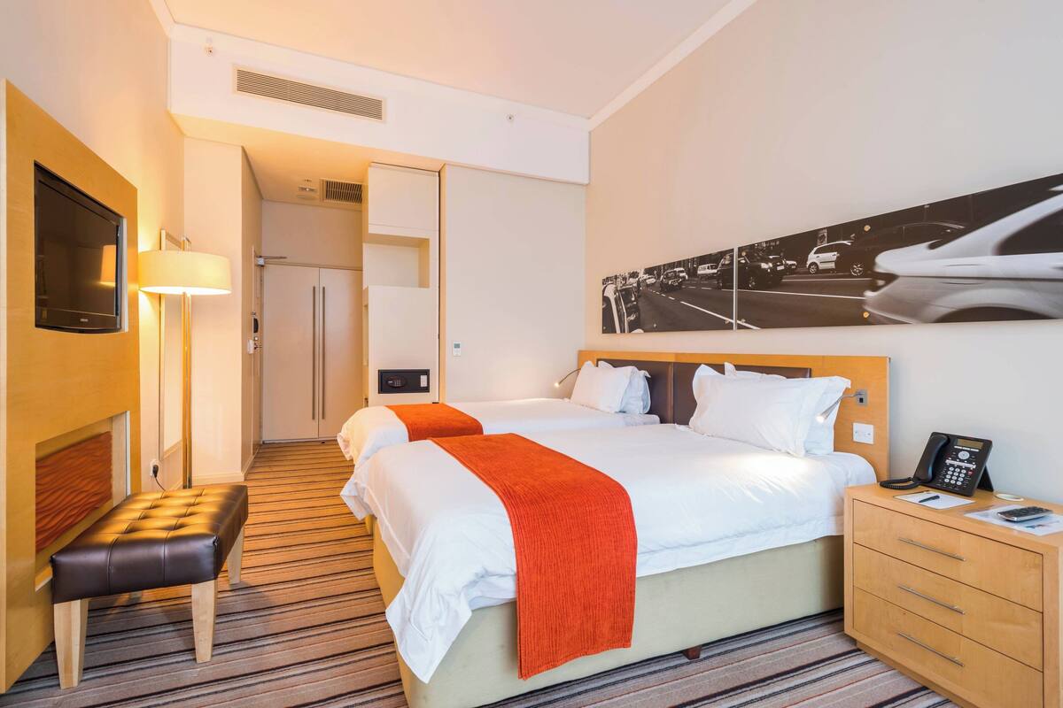 Una habitación de hotel con cama, mesitas de noche, televisión y un cuadro en la pared.