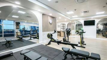 A modern gym with various exercise equipment, large windows, and a visible clock on the wall.