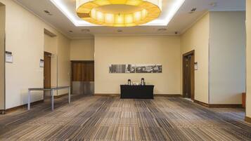 A spacious hallway with a patterned carpet, a black reception desk, and a cityscape artwork on the wall.