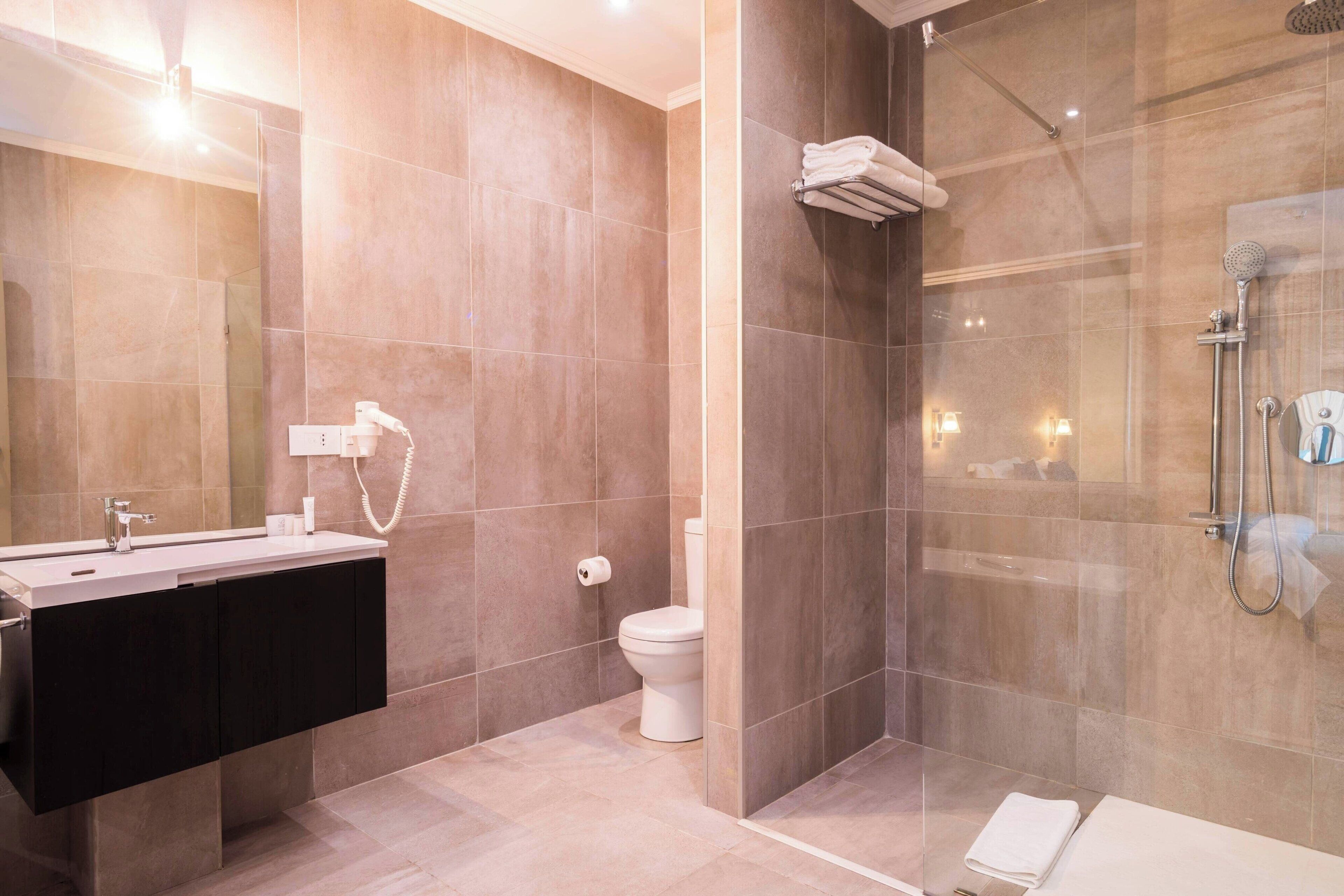 A modern bathroom with a dual sink vanity, a toilet, a glass-enclosed shower area, and a bathtub.