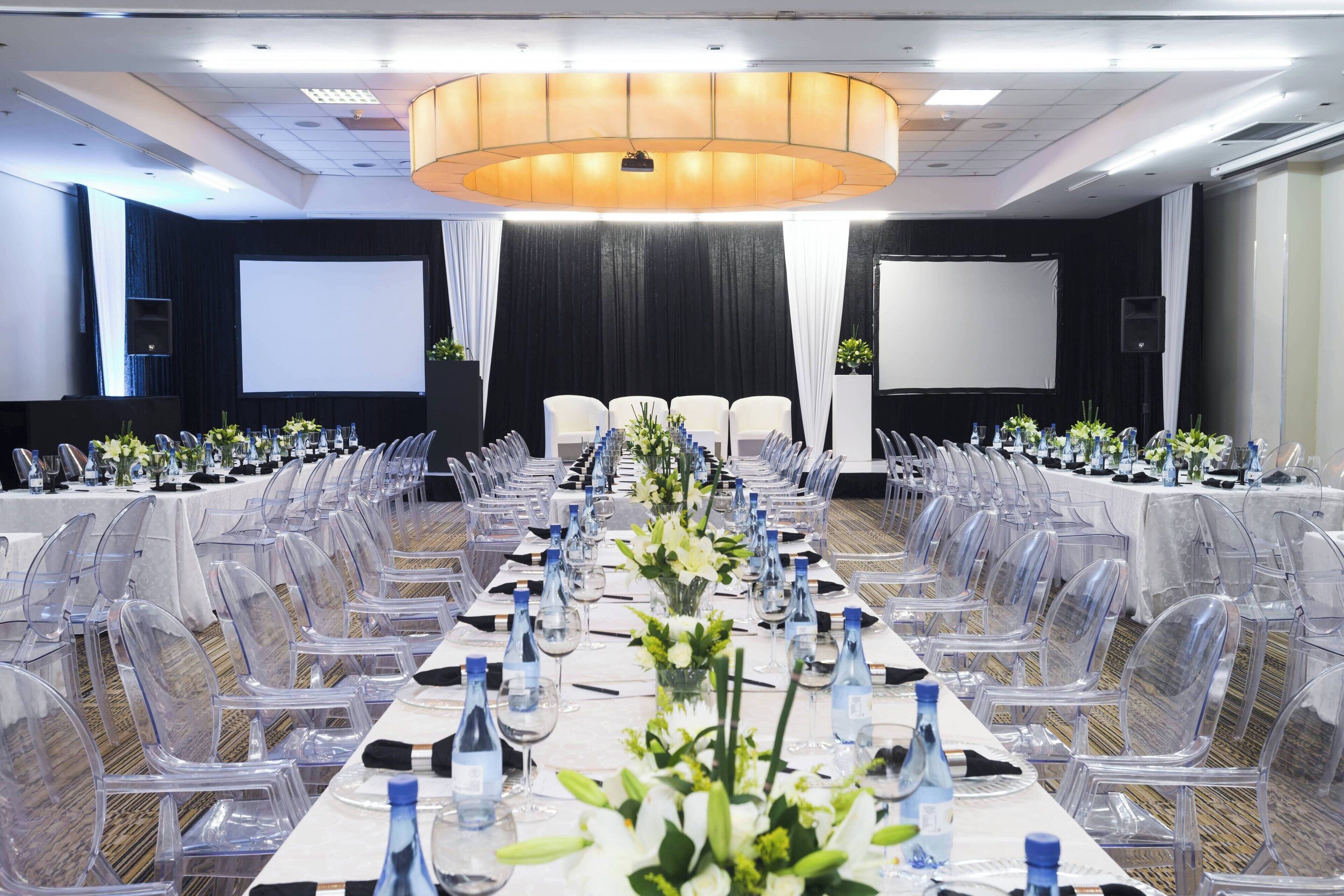 A conference room with a long table, clear chairs, and a projector screen.