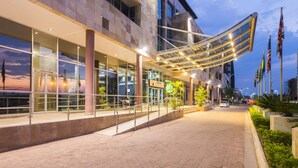 A modern building with a glass facade, outdoor seating area, and a covered walkway. - Protea Hotel by Marriott Gaborone Masa Square (Gaborone)