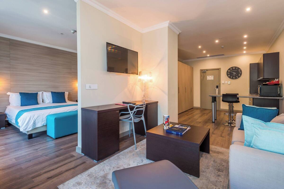 Una habitación de hotel moderna con cama, escritorio, silla, sofá y una pequeña kitchenette.