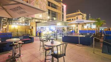 An outdoor dining area with tables and chairs, umbrellas, and a bar area with a sign for Absolut Vodka.