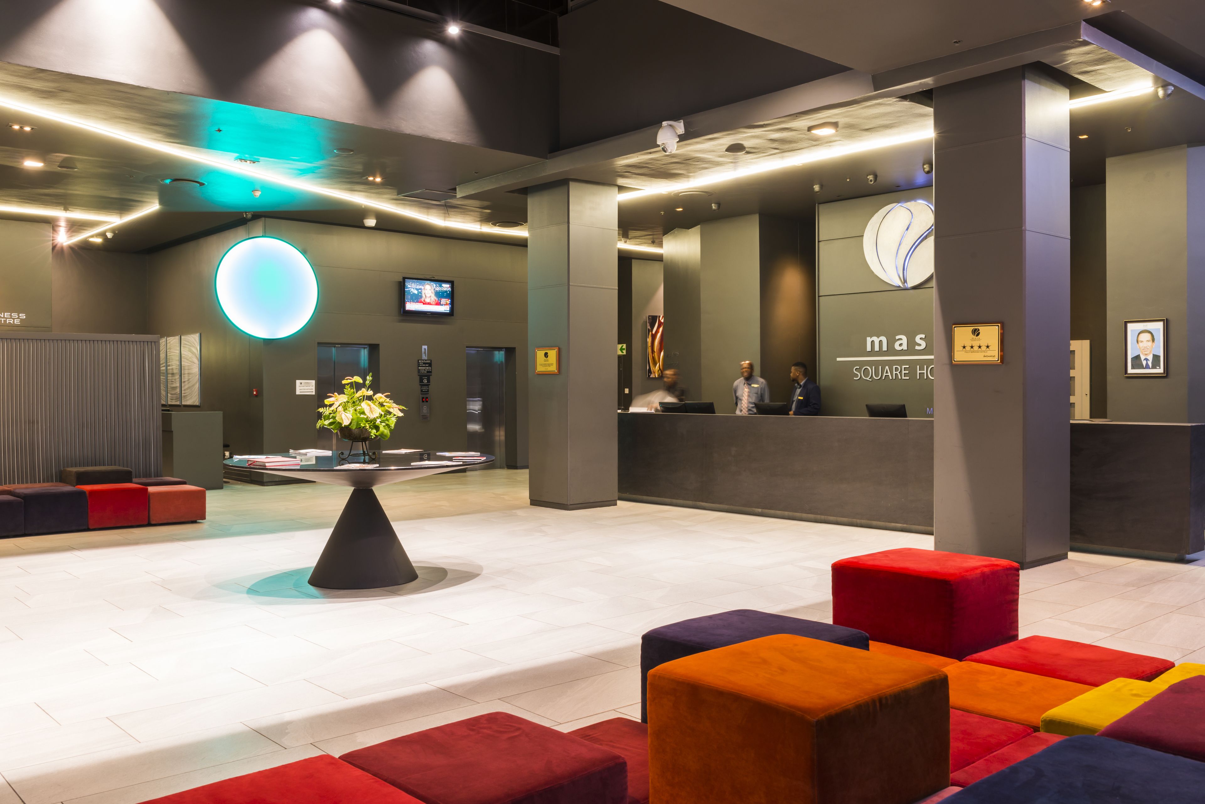 A modern hotel lobby with a reception desk, colorful seating areas, and a large illuminated wall feature.