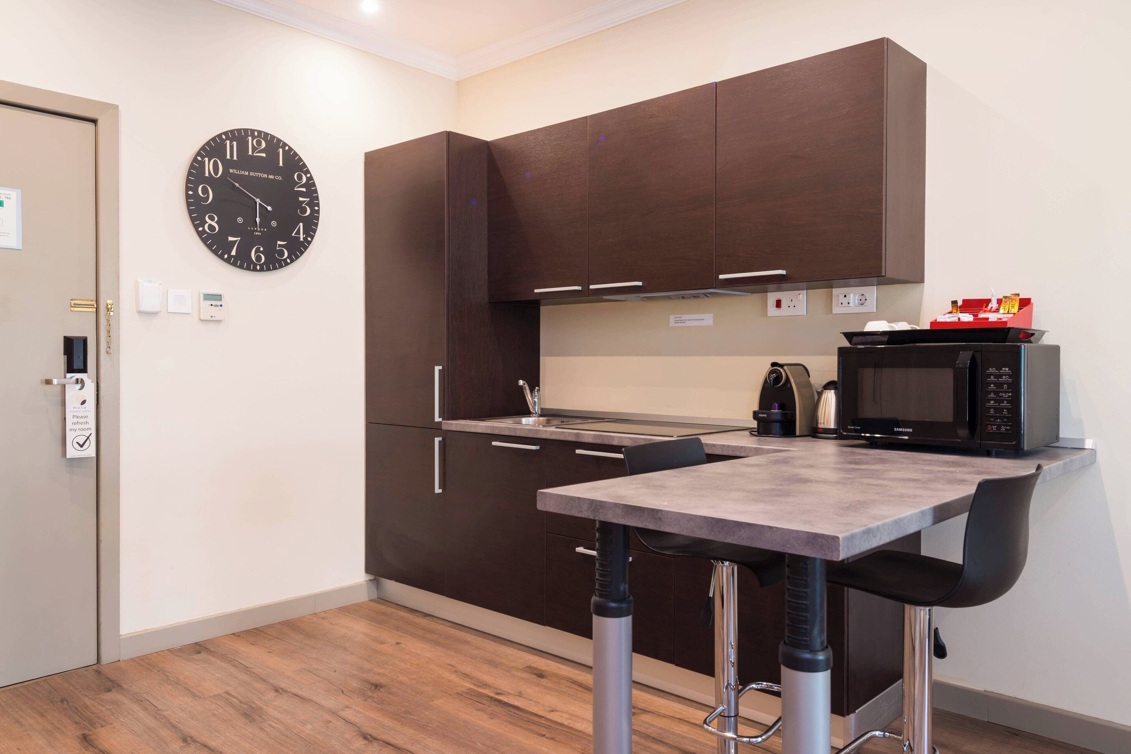 A modern kitchen with dark cabinets, a microwave, and a clock on the wall.