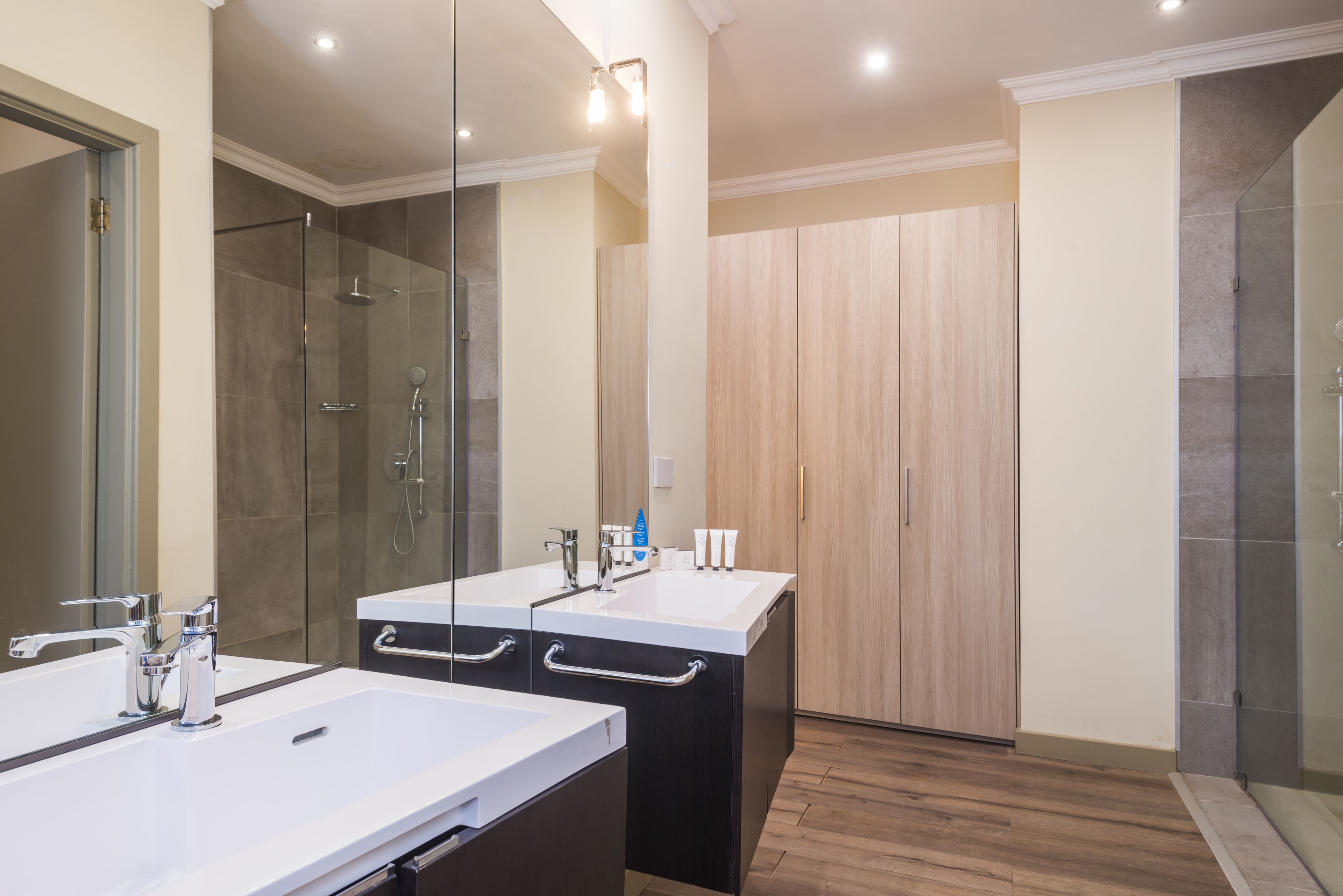 A modern bathroom with two sinks, a glass shower enclosure, and a wooden wardrobe.