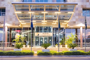 A modern hotel entrance with glass doors, a sign reading "Masa Square Hotel," and potted plants in front.