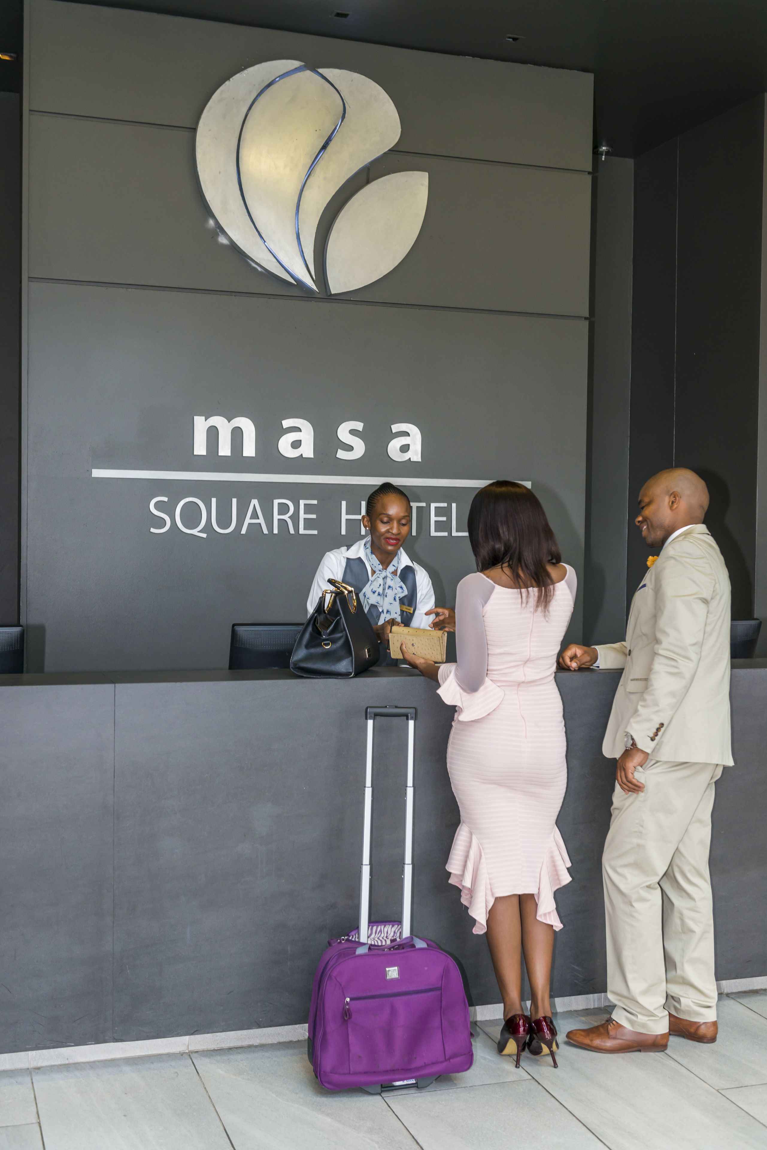 A reception desk at the MSA Square Hotel with a modern logo, a reception area, and a purple suitcase on the floor.