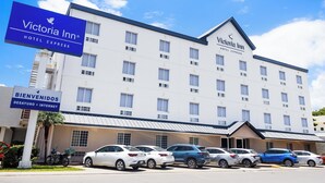Un bâtiment de plusieurs étages abritant un hôtel Victoria Inn Hotel Express, avec une façade blanche, de nombreuses fenêtres et un parking où sont stationnées plusieurs voitures.
