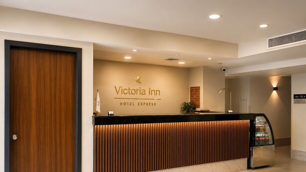 Un comptoir d’accueil d’hôtel avec un revêtement en bois, une enseigne indiquant « Victoria Inn Hotel Express », et un panneau de signalisation indiquant les numéros de chambre.