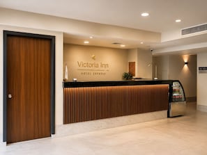 Un mostrador de recepción de hotel con detalles de madera, un letrero que dice 'Victoria Inn Hotel Express' y una señal indicando los números de las habitaciones.