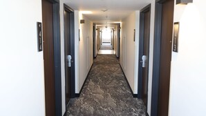 Un couloir d’hôtel avec un sol en marbre, des portes de chaque côté et une lumière au bout.