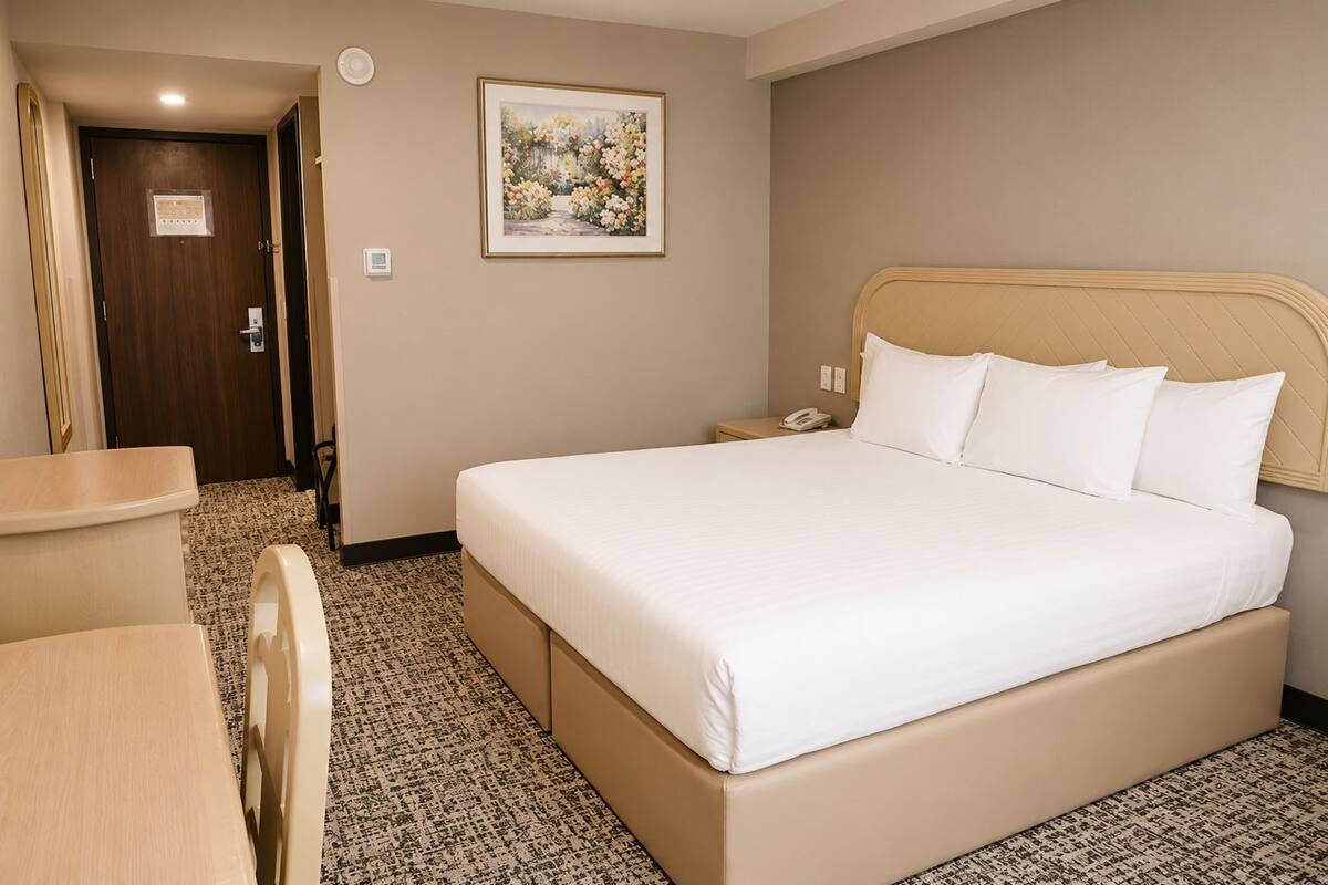 A hotel room with a bed, bedside table, chair, and a painting on the wall.