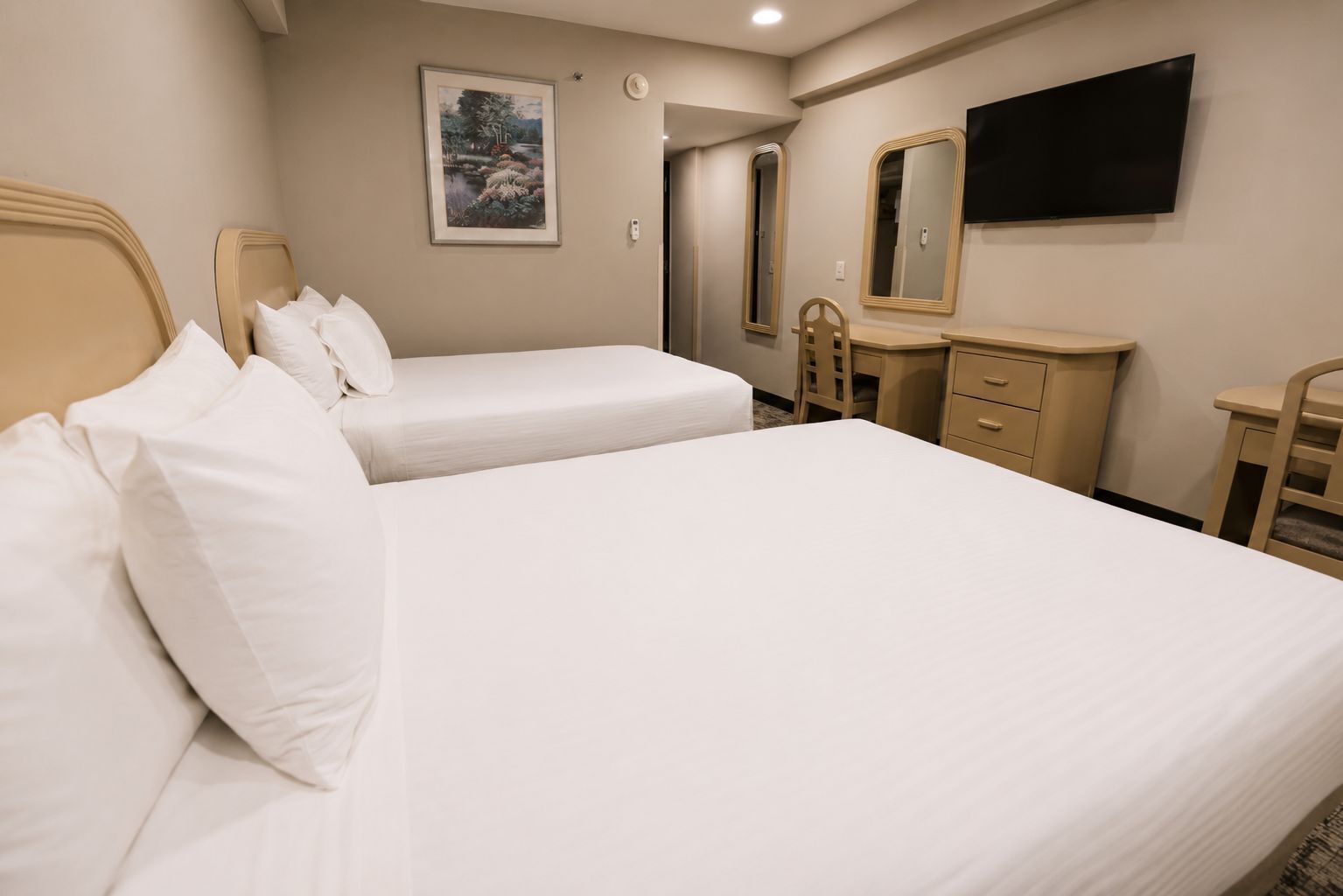 A hotel room with two beds, a bedside table, a dresser, a mirror, and a TV mounted on the wall.