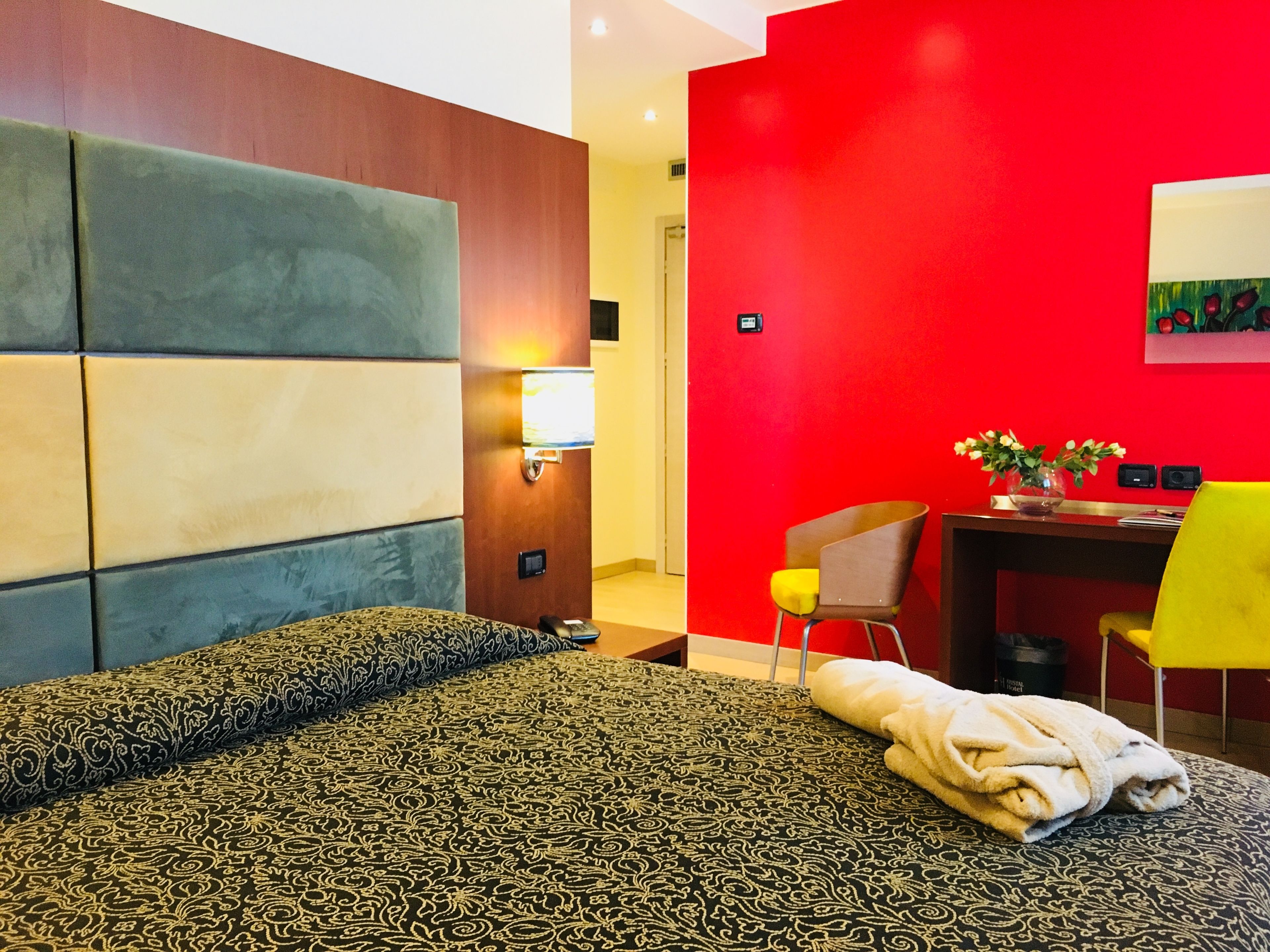 Habitación de hotel con una cama, un escritorio y una silla. La pared es roja y el cabecero de madera.